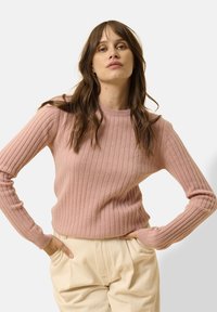 Suéter de punto acanalado en rosa suave, con mangas largas y cuello redondo, combinado con pantalones color crema.
