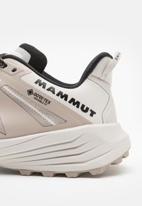 Leichter Laufschuh in Beige und Weiß mit texturiertem Obermaterial, schwarzen Akzenten, GORE-TEX-Branding und einer robusten Sohle für Trittfestigkeit.
