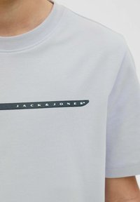 Šviesiai pilkas medvilninis marškinėlis su apvaliu kaklu; turi tamsiai mėlyną horizontalią juostą ir baltą "JACK & JONES" logotipą. Trumpomis rankovėmis, lygia tekstūra.