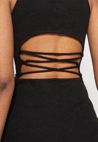 Gros plan d'une personne portant une robe noire avec un dos ouvert et des fines bretelles croisées.