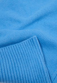 Tecido de suéter de malha azul claro com uma textura suave, apresentando um punho canelado e um corpo liso para uma aparência acolhedora.