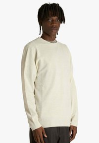 Maglione lavorato a maglia color crema, con scollo rotondo e maniche lunghe, con polsini e orlo a coste. Vestibilità comoda, tessuto morbido.