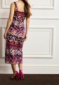 Blumendruckkleid mit verstellbaren breiten Trägern, tailliertem Oberteil und knielangem Rock auf dunklem Hintergrund, kombiniert mit rosa High Heels.