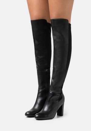 Bottes en cuir noir au-dessus du genou avec un talon épais, présentant une texture lisse et un détail de fermeture éclair sur le côté pour un enfilage facile.