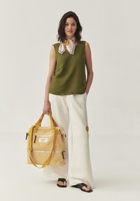 Top sin mangas verde oliva, pantalones de pierna ancha crema, bolsa amarilla a rayas con detalles de cremallera, acento floral en los pantalones, sandalias deslizantes negras.