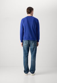 Felpa blu reale con polsini e orlo a costine, abbinata a jeans in denim blu chiaro. L'outfit è completato da sneakers bianche.