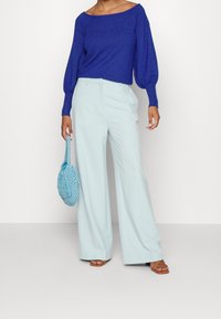 Dlouhé světle modré kalhoty s širokými nohavicemi spárované s masivním královsky modrým pleteným svetrem a texturovanou světle modrou kabelkou. Outfit doplňují hnědé sandály.