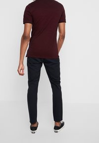 T-shirt bordeaux à manches courtes avec bordure noire, associé à un pantalon noir et des baskets noires. Coupe décontractée, tissu lisse, design simple.