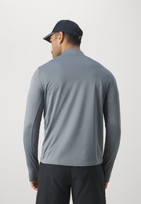 T-shirt de sport à manches longues, gris clair, fabriqué en tissu lisse et flexible. Il présente un col rond et des détails de couture minimalistes.