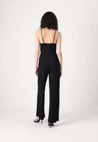 Crni kombinezon s tankim bretelicama, uskim strukom i širokim nogavicama. Izrađen od glatkog, teksturiranog materijala s blagim sjajem.