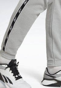 Grå texturerade joggingbyxor med svart och vit randdetalj; bärs med svart och vita sportskor med nätdetaljer.