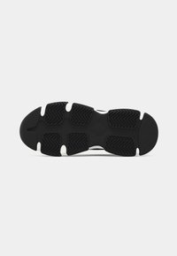 Suela de zapatilla en blanco y negro con secciones de goma texturizada para agarre y patrones de tracción en zigzag.