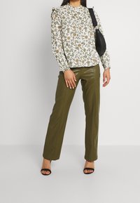 Blouse blanche à motifs floraux verts et oranges, épaules froncées ; pantalon vert olive en cuir synthétique ; talons noirs à lanières ; sac à bandoulière noir.