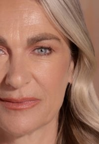 Nahaufnahme eines Gesichts mit glatter Haut, hellgrauen Haaren, blauen Augen und dezentem Make-up, das eine sanfte rosa Lippenfarbe zeigt.