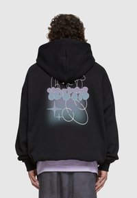 Felpa nera con cappuccio e una grande grafica pastello che riporta la scritta "YOUTH" sul retro, caratterizzata da contorni curvi e accenti a forma di stella. Vestibilità morbida e oversize.