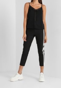 Camisole noire à bordure en dentelle associée à un pantalon noir fuselé avec des bandes blanches sur les côtés, complétée par des baskets blanches épaisses.