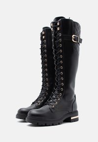 Czarne, skórzane botki za kolano z wiązaniem, ozdobione złotymi oczkami, z pikowanym tyłem i masywną podeszwą z złotym akcentem.