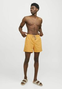Shorts de bain orange avec une taille élastique et un cordon de serrage, présentant une coupe décontractée et un design simple. Portés avec des sandales marron.