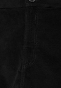 Svart kordfloret material med en slät yta och vertikala ribbor, med en knapp och kontrasterande sömnad längs sömmen.