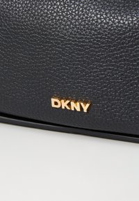 Fekete textúrájú bőrtáska fényes arany DKNY logóval. Simább felülettel és diszkrét, domborítással készült mintázattal rendelkezik.