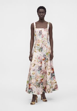 Femme portant une robe sans manches à encolure carrée, longue jusqu'au sol, avec un motif floral pastel et des talons ouverts beiges.