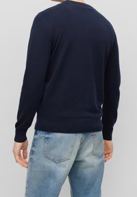 Suéter de punto azul marino con mangas largas y puños acanalados. Presenta un cuello redondo clásico y un dobladillo ajustado, combinado con jeans de mezclilla azul claro.