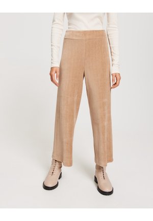 Beige corduroy wide-leg pants with a high elastic waistband; textured fabric and soft finish, paired with light-colored boots.