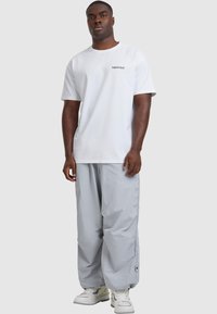 Valge puuvillane t-särk, mille rinnal on trükitud "unustatud ajad", koos laia lõikega heledate hallide nailonpükstega ja valgete tossudega.