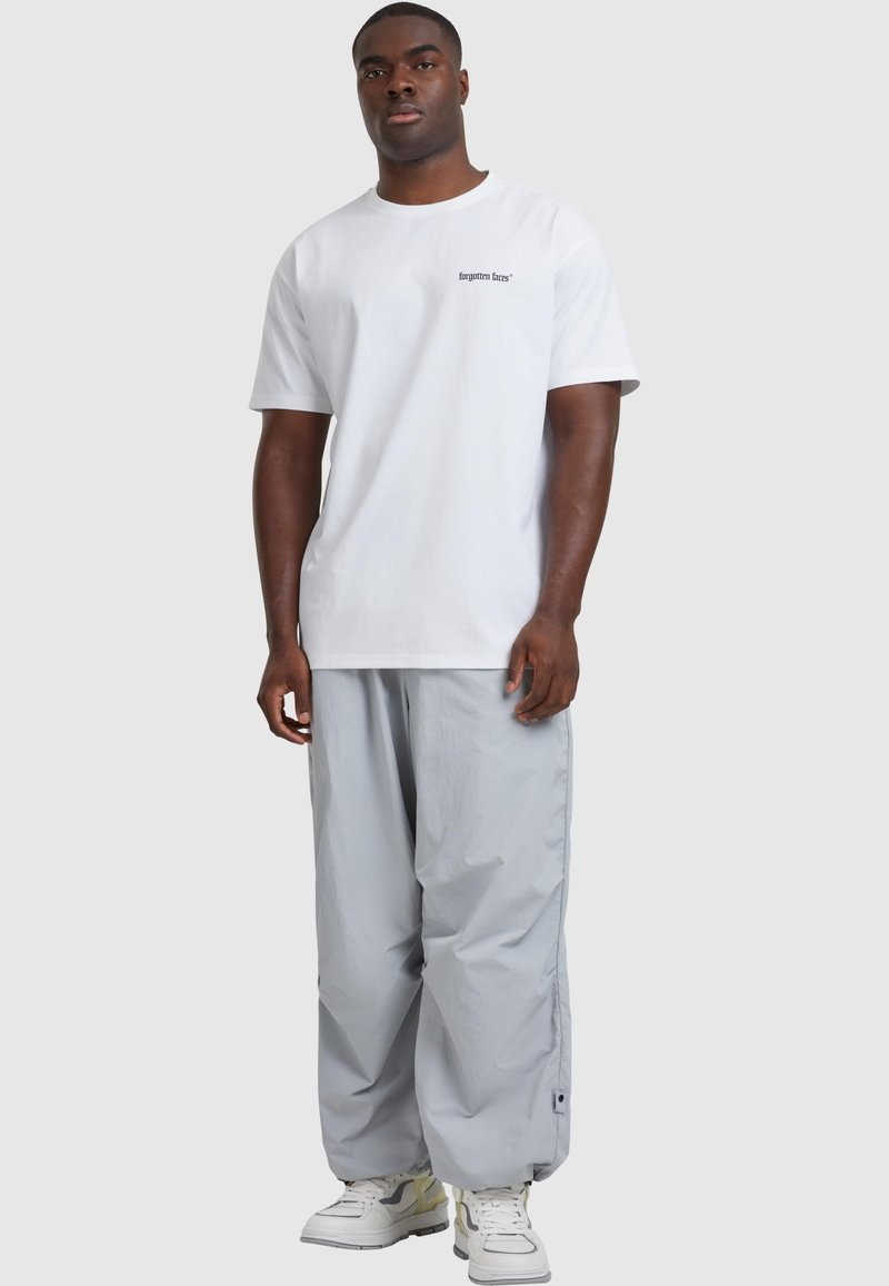 Valge puuvillane t-särk, mille rinnal on trükitud "unustatud ajad", koos laia lõikega heledate hallide nailonpükstega ja valgete tossudega.