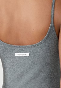 Graues Tanktop mit rundem Ausschnitt und dünnen Trägern, mit einem Label "Cool Cosy Comfy", das hinten eingenäht ist.