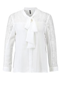 Blusa bianca con maniche in pizzo, fiocco al collo, chiusura frontale con bottoni e una texture di tessuto liscia. Il pizzo presenta motivi intricati.