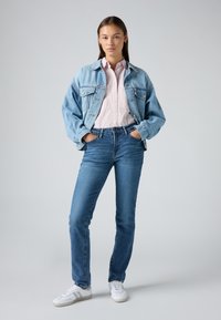 Denim jacket in light blue, featuring oversized fit and button closure. Paired with light blue jeans and white sneakers with grey accents.