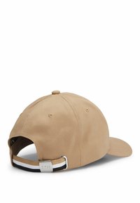 Cappellino di cotone beige con cinturino regolabile, dotato di un accento metallico argento e una banda a righe nere e bianche sul retro.