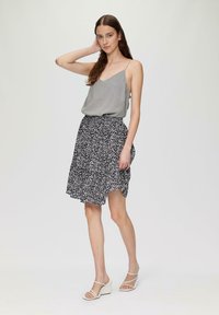 Graue Spaghettiträgershirt kombiniert mit einem schwarzen Rock mit Blumenmuster, der eine ausgestellte Form und einen seitlichen Schlitz hat. Keil-Sandalen.