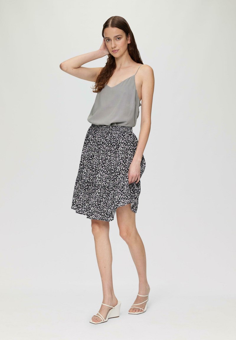 Graue Spaghettiträgershirt kombiniert mit einem schwarzen Rock mit Blumenmuster, der eine ausgestellte Form und einen seitlichen Schlitz hat. Keil-Sandalen.