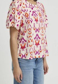 Short-sleeve top featuring a lightweight, textured fabric with orange, pink, and purple ikat patterns on a light cream background.