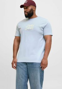 Lyseblå T-shirt med korte ærmer og rund hals, med "Jack & Jones" logo i gul print på brystet. Båret med blå jeans.