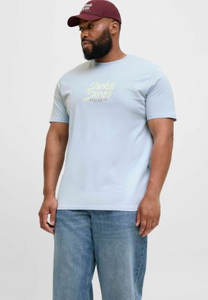 Lyseblå T-shirt med korte ærmer og rund hals, med "Jack & Jones" logo i gul print på brystet. Båret med blå jeans.