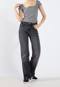 Black high-waisted jeans with a straight-leg cut, paired with a checkered short-sleeve top. The outfit is completed with black sneakers.