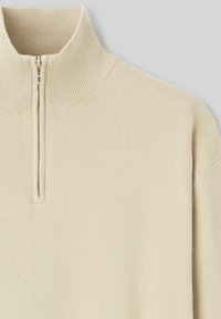 Pull en beige clair à zip, avec un col haut, une texture côtelée et une finition lisse. Il dispose d'un zip quart de longueur et d'une coupe décontractée.