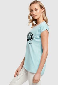 T-shirt di cotone azzurro chiaro con maniche arrotolate, caratterizzata da una stampa grafica nera di un codice a barre e un design animale sulla parte anteriore.