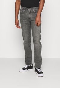 Šedé džíny z denimu se rovný fit, s knoflíkovým zapínáním, poutky na pásek a bledým omakem. Kombinované s černými teniskami.