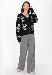 Fekete kardigán ezüst virágmintás hímzéssel, gombos záródással és hosszú ujjal, szürke, bő szárú nadrággal párosítva. Sima textúra, laza szabás.