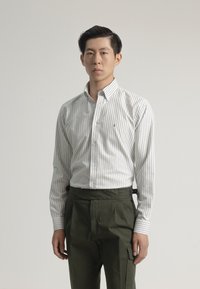 Camisa de botones a rayas blancas y grises con cuello, combinada con pantalones de tiro alto en color verde oliva con herrajes ajustables.