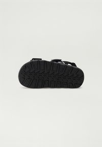 Svarte sandaler med en teksturert gummisåle med et godt grep. To justerbare stropper over toppen for sikker passform.
