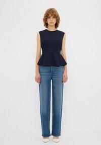 Top peplum navy a maniche corte, abbinato a jeans dritti azzurri chiari e scarpe bianche con punta a punta. Tessuto morbido, vestibilità sartoriale.