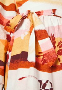 Ceinture en tissu nouée en un nœud sur une jupe avec un motif abstrait à blocs de couleurs orange, rose, rouge et crème, ainsi qu'un motif floral.