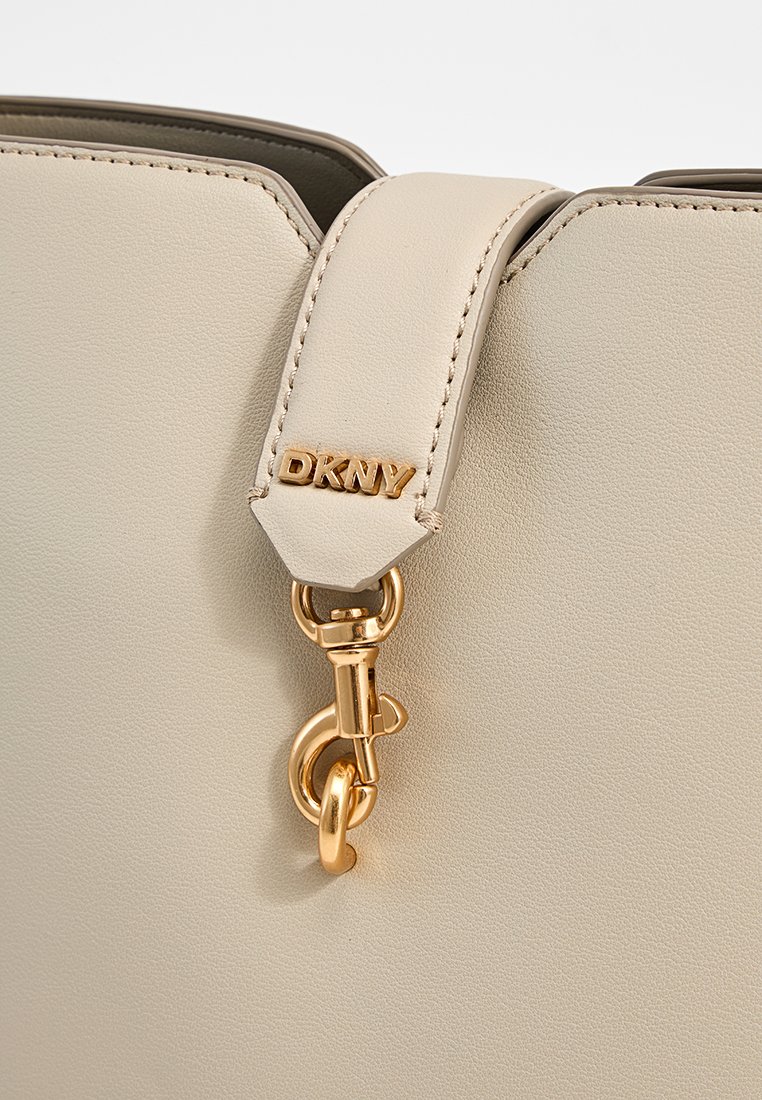 DKNY-Handtasche aus beigem Leder, mit einem goldfarbenen Metallclip und einem Riemen mit genähten Details. Glatte Textur mit dezentem Branding.