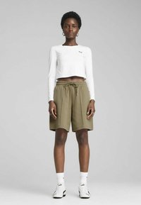 Top blanco recortado de manga larga con un logo, combinado con pantalones cortos verdes oliva con cinturilla elástica y bolsillos laterales. Zapatillas blancas.