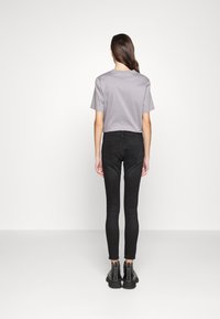 Camiseta gris de manga corta combinada con jeans skinny negros y botas tobilleras negras. Tejido suave, diseño ajustado y jeans con puños.